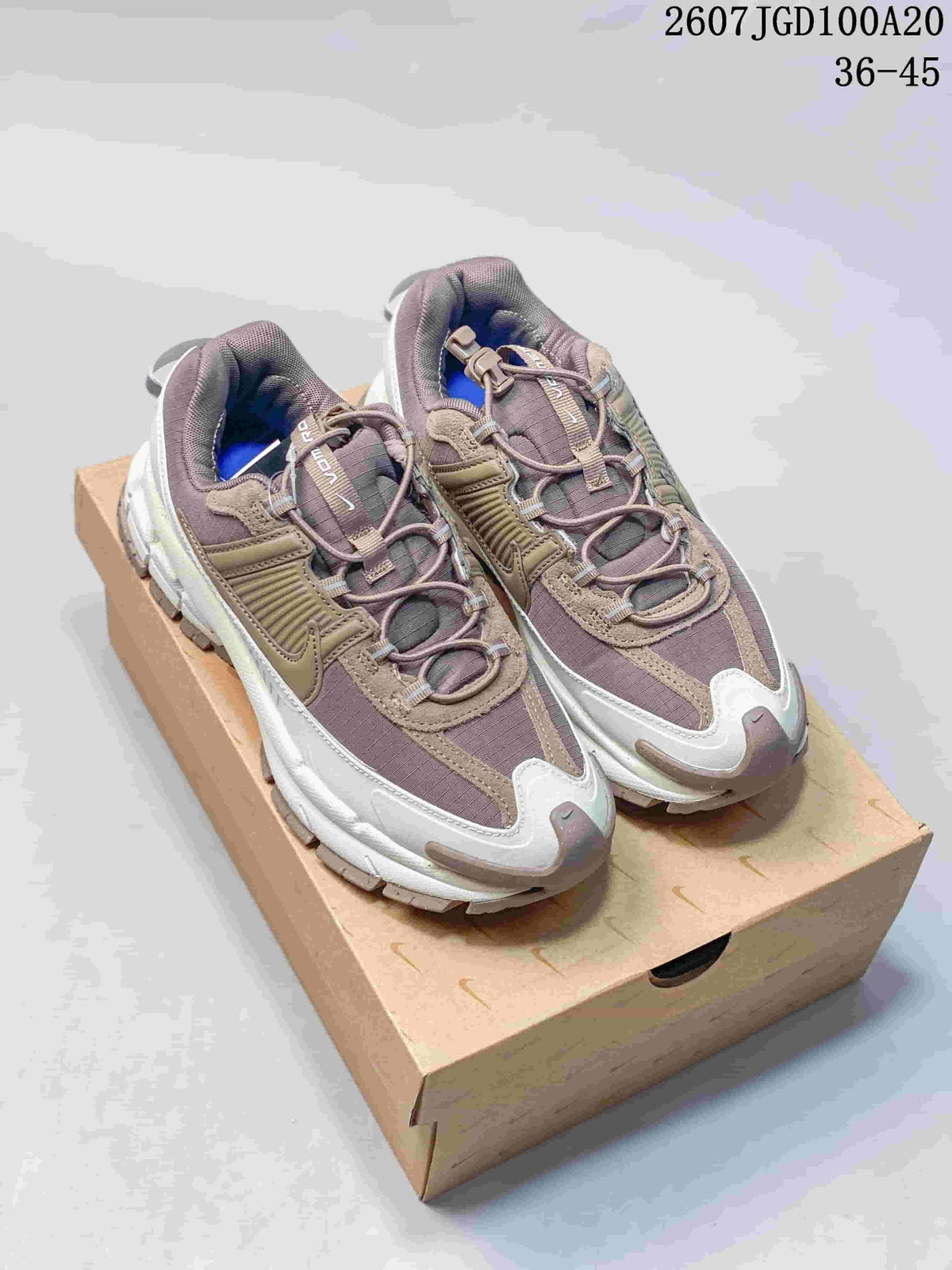 Pair of taupe-gray and white Nike Zoom Vomero Roam sneakers displayed on a shoebox, with the style code and size range visible above.