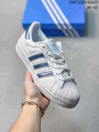 Angled side view showing the shell toe, blue stripes, Superstar side branding, and blue heel tab.