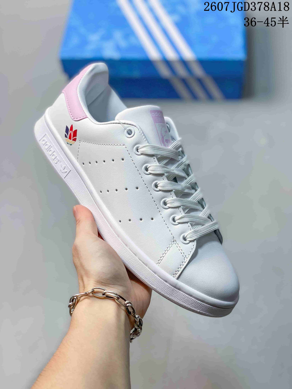 Angled side view showing the white sneaker, pink heel detail, multicolor adidas trefoil accent, and textured outsole.