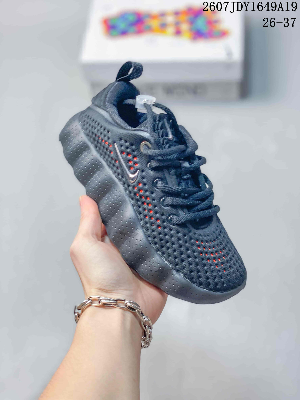 Dark Nike Mind 002 kids sneaker with orange accents visible through the perforations.
