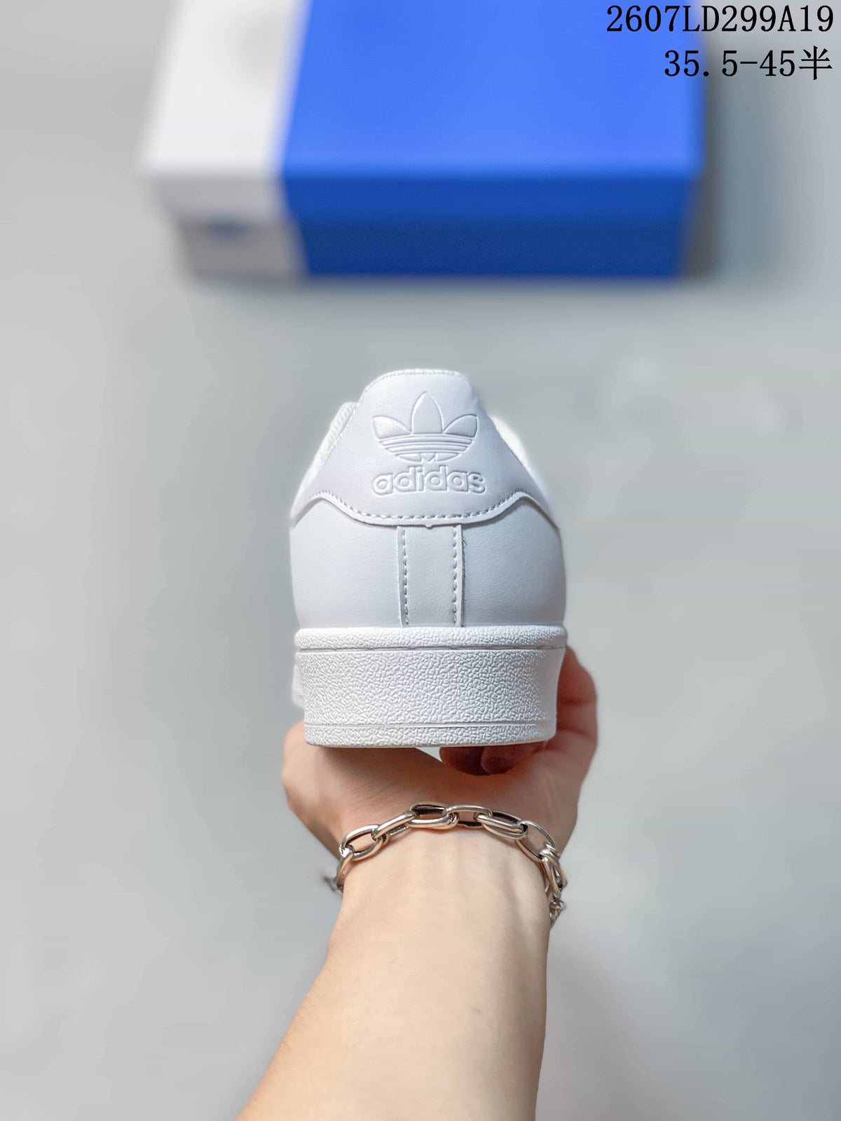 Rear view of a white sneaker showing the Adidas Trefoil heel branding and layered white sole.