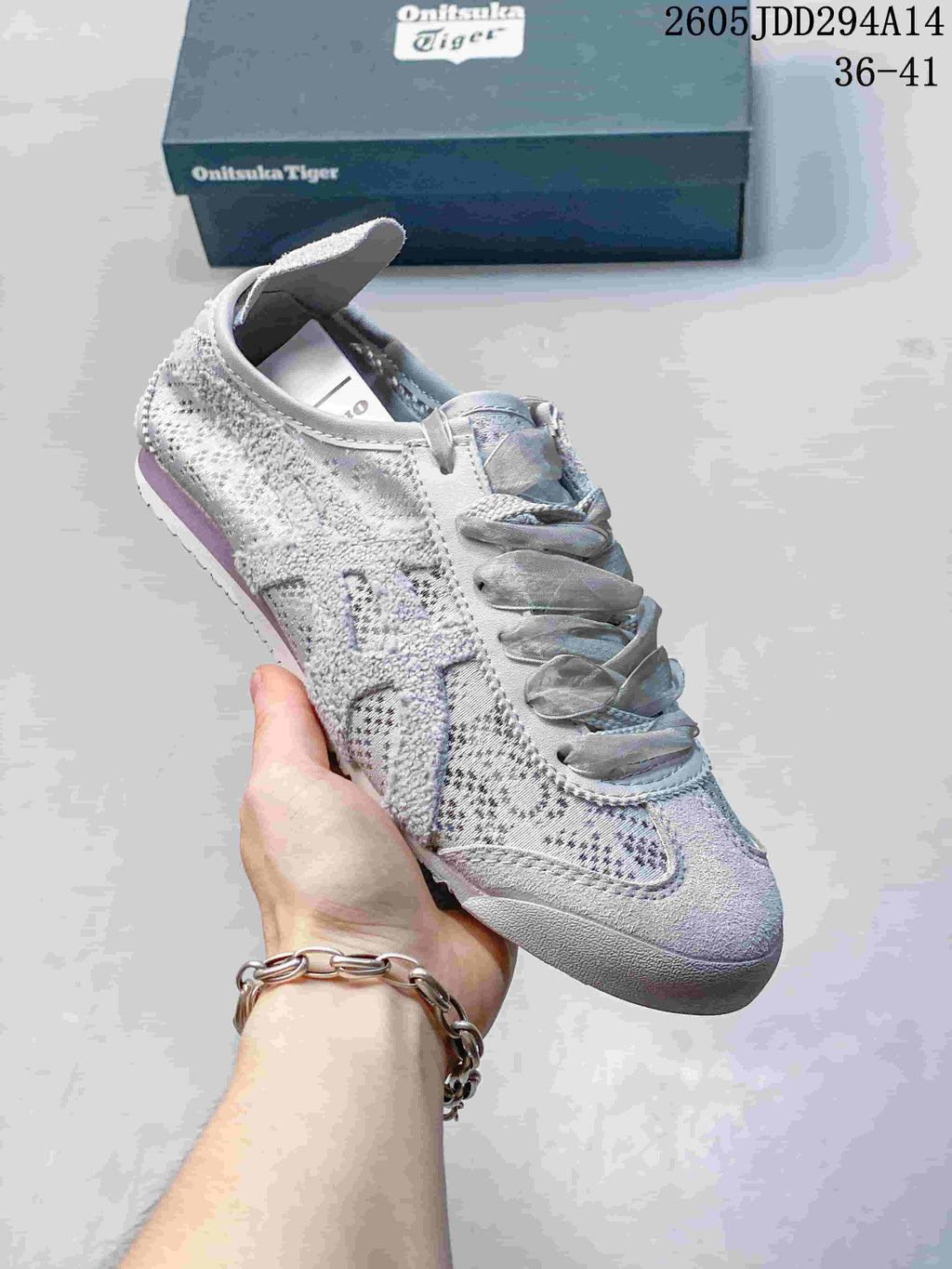 Angled side view of the light gray Onitsuka Tiger sneaker showing the patterned textile upper, layered side panels, and rubber outsole.