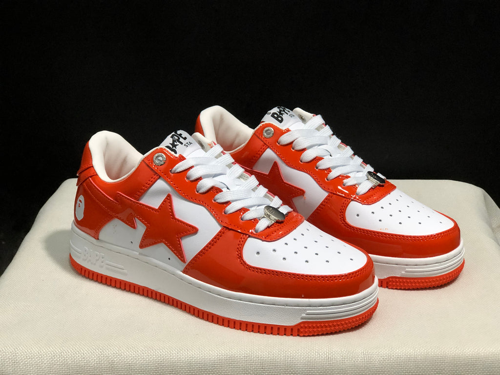 Three-quarter view of the white and orange BAPE Sta sneaker pair with visible side stars and perforated toe boxes.