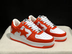 Three-quarter view of the white and orange BAPE Sta sneaker pair with visible side stars and perforated toe boxes.