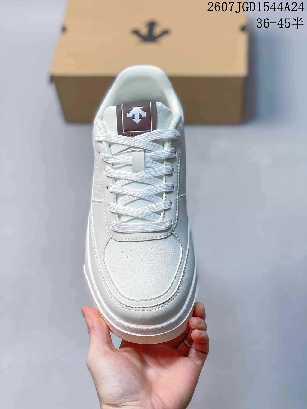 Top view of the white sneaker showing white laces, a padded tongue with brown branding detail, and a layered toe panel.