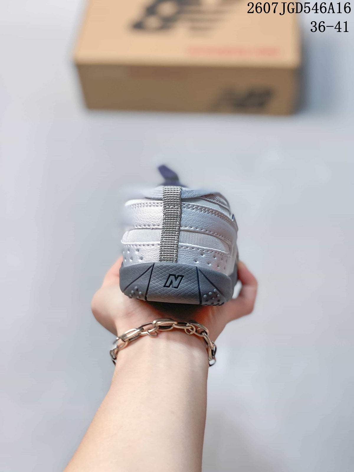 Rear view of the silver-gray shoe showing the New Balance logo on the dark heel outsole and layered upper panels.
