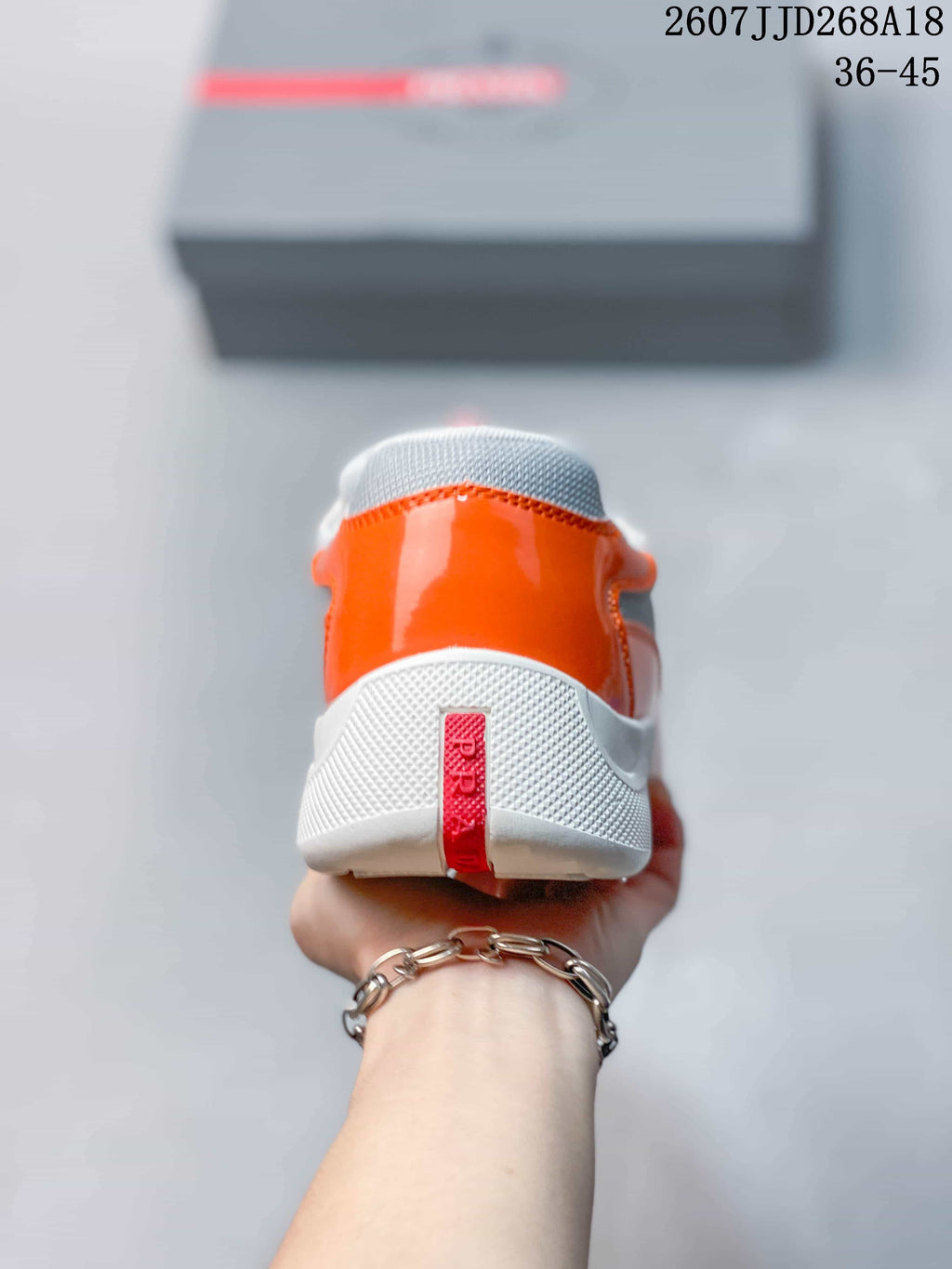 Rear view of the orange and gray sneaker showing the padded heel, textured gray panel, and red branding strip.