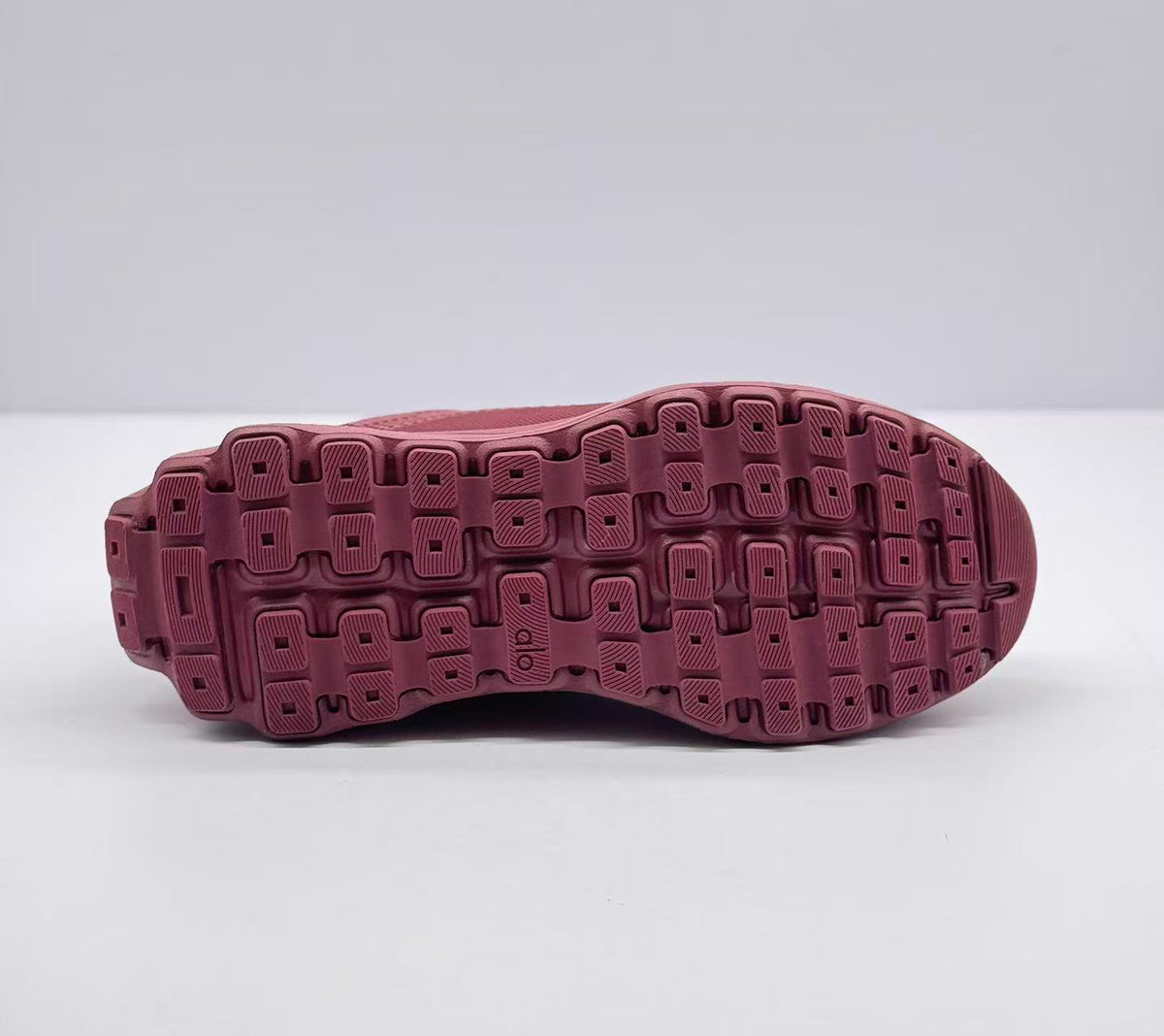 Underside view showing the burgundy patterned rubber outsole with segmented traction blocks.