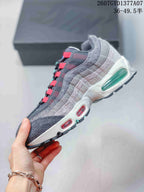 Side profile of a grey Nike Air Max 95 sneaker with layered detailing, red Air windows, and a translucent green heel unit.