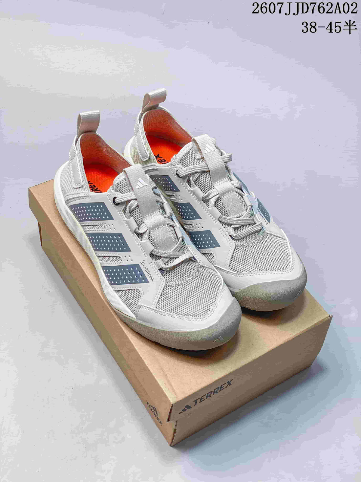 Pair of light gray Adidas Terrex shoes with dark gray side details, orange lining, and lace-up fastening, shown on a box.