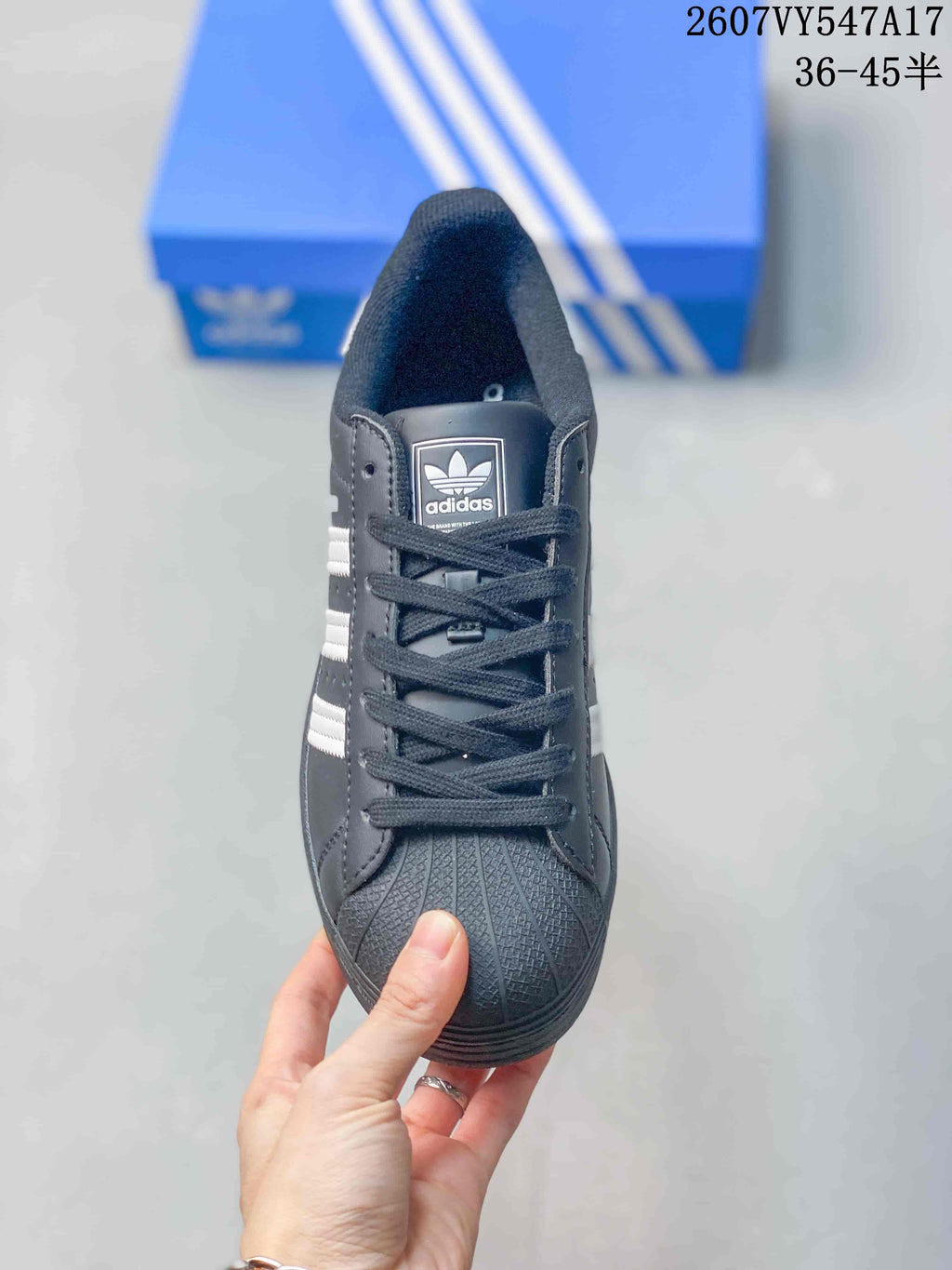 Front view of a black Adidas Superstar sneaker showing black laces, a textured shell-toe front, and Adidas tongue branding.