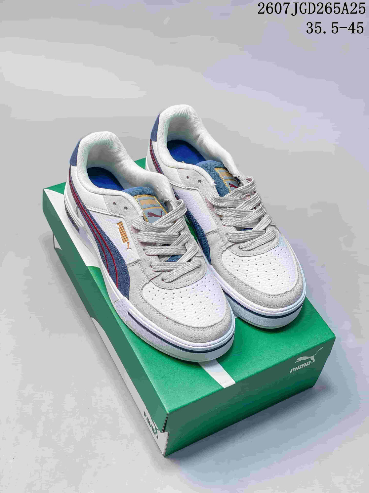 Pair of white PUMA CA Pro low-top sneakers with navy and red accents displayed on a green shoebox.