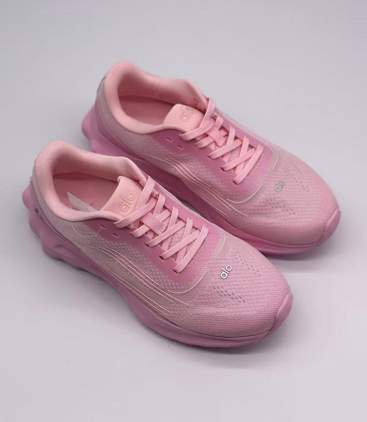 Top three-quarter view of the pink Alo sneaker pair showing the padded collars and lace layout.
