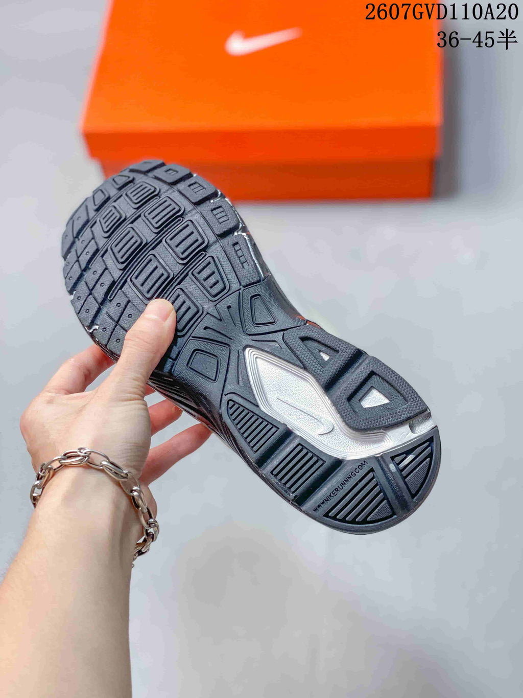 Underside view of the sneaker showing the black-and-grey outsole with a segmented traction pattern; style code and size range appear in the background.