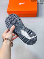 Underside view of the sneaker showing the black-and-grey outsole with a segmented traction pattern; style code and size range appear in the background.