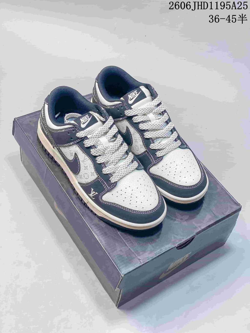 Pair of white and navy low-top sneakers with dark patterned laces, shown on a box.