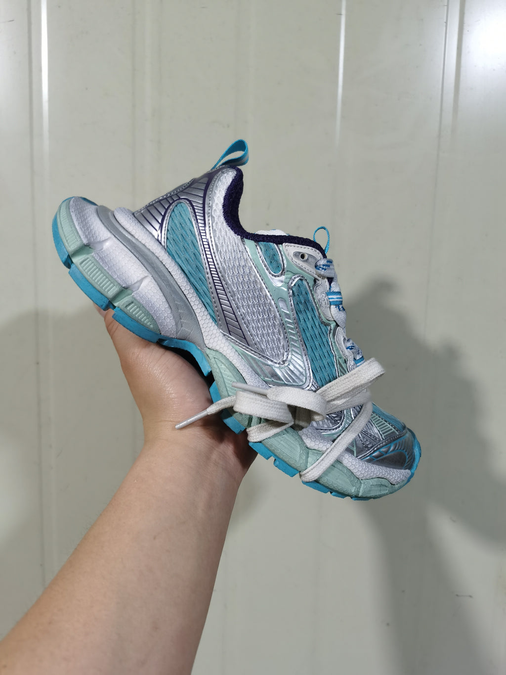 Angled view of the sneaker showing the layered side construction, lace-up front, padded collar and contrasting blue outsole.