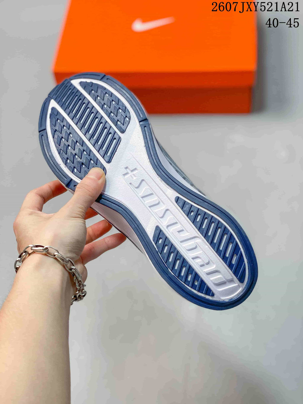Underside view of a navy and white sneaker showing the patterned rubber outsole and raised midfoot branding.