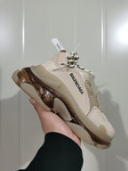 Side view of a nude Balenciaga Triple S sneaker with visible Balenciaga branding, mesh inserts, patterned laces, and a sculpted translucent sole.