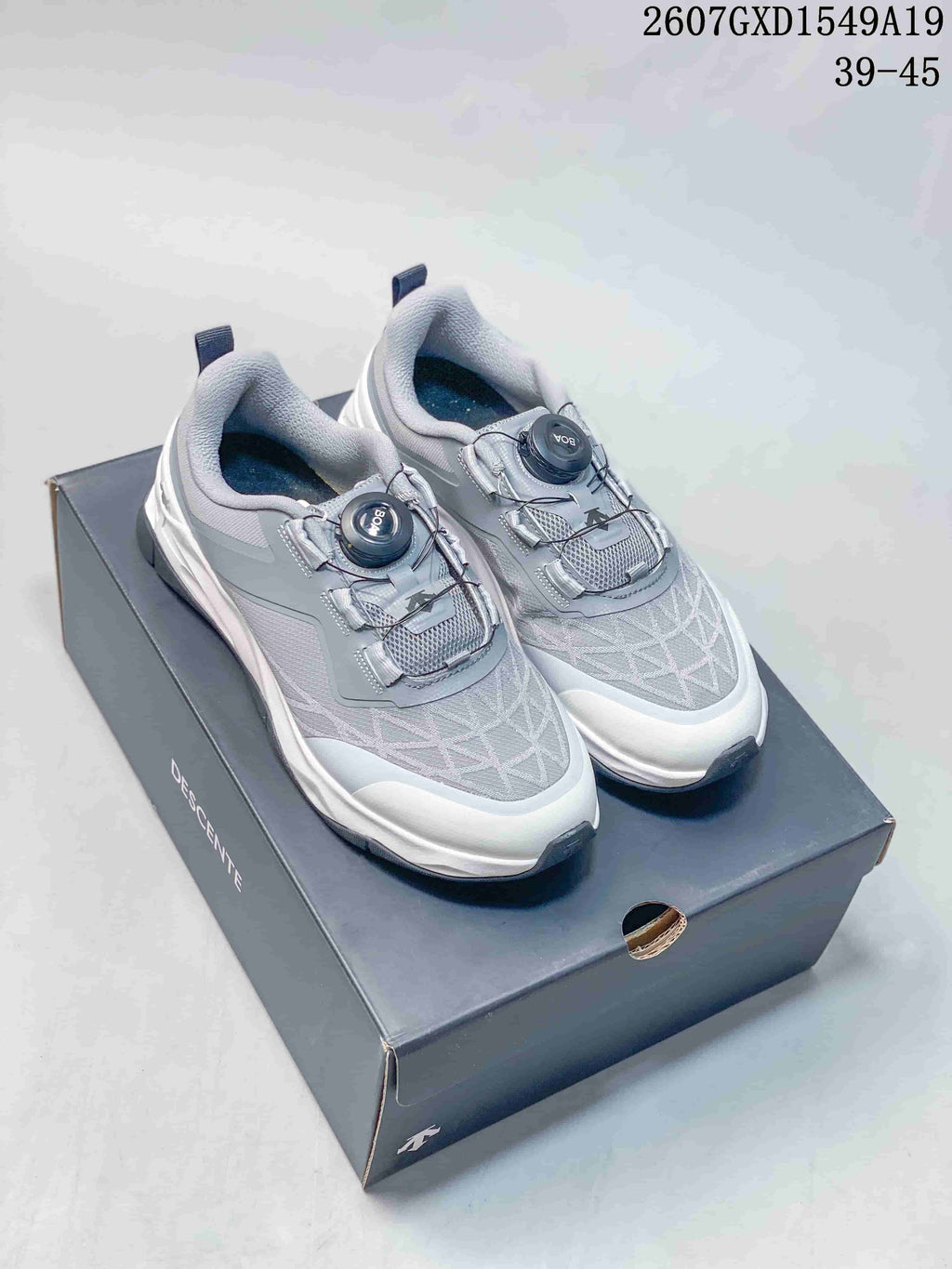 Pair of grey and white Descente Circuit 2.0 Wire sneakers displayed on a shoebox, showing the dial closures and patterned uppers.