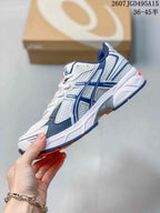 Side view of the ASICS GEL-1130 sneaker showing white mesh-style panels, navy overlays and orange outsole accents.