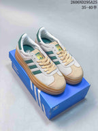 Pair of white and green Adidas Gazelle Bold sneakers displayed on a blue Adidas shoe box, showing the layered gum-colored platform sole.