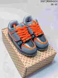 Pair of gray and black Louis Vuitton Trainer Maxi sneakers with orange laces displayed on a branded shoebox.