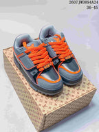 Pair of gray and black Louis Vuitton Trainer Maxi sneakers with orange laces displayed on a branded shoebox.