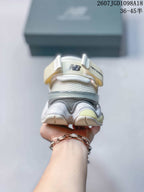 Rear view of a white and grey New Balance 9060 sneaker showing the layered heel structure, pull tab and pale yellow outsole accents.