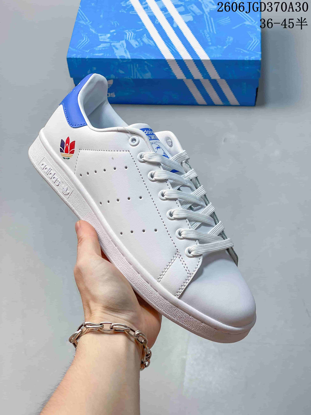 White Stan Smith-style sneaker with a multicolor heel emblem and a blue heel tab.