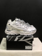 Side view of the white and grey sneakers on the box, showing layered panels, directional side graphics, and chunky soles.