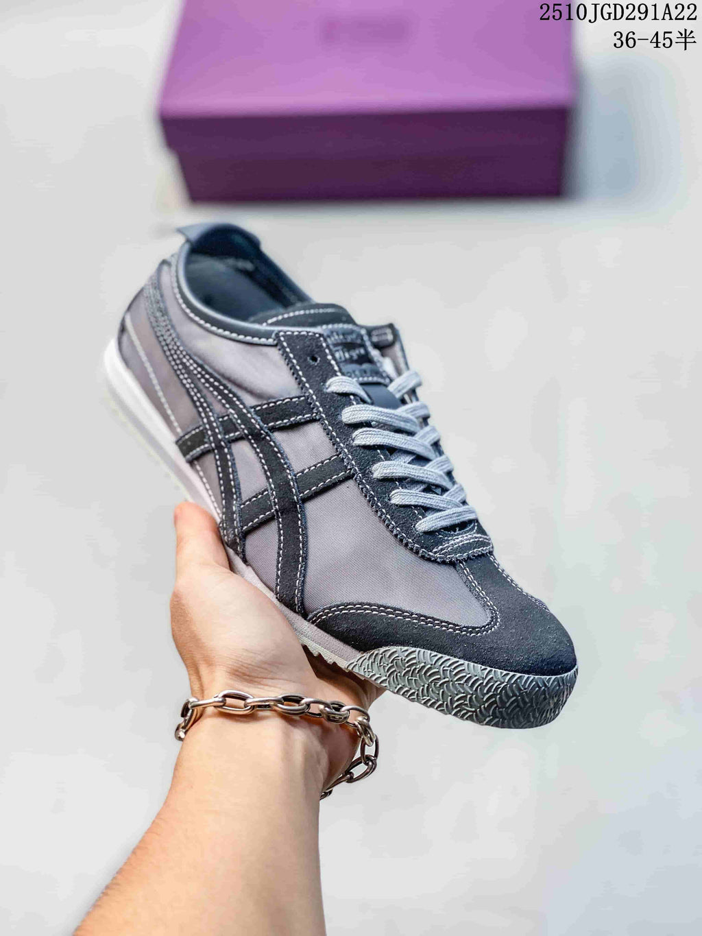 Black and gray Onitsuka Tiger sneaker held in hand, showing contrast stripes, stitched panels, laces and a textured outsole.
