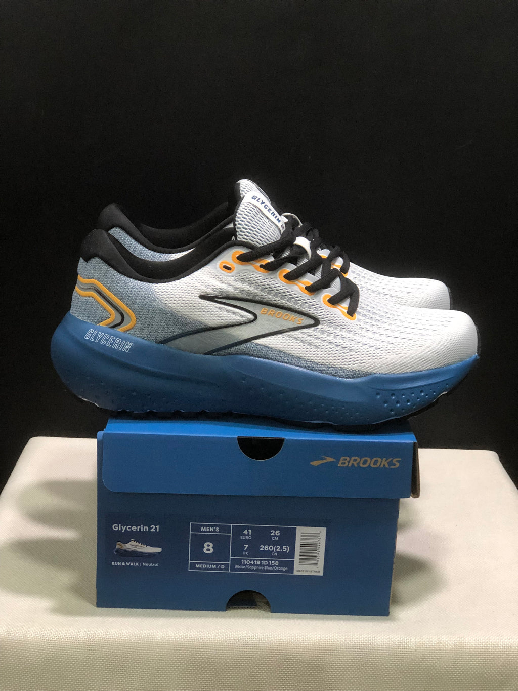Side view of the white and blue Brooks Glycerin 21 sneakers with orange accents, displayed on a Brooks shoebox.
