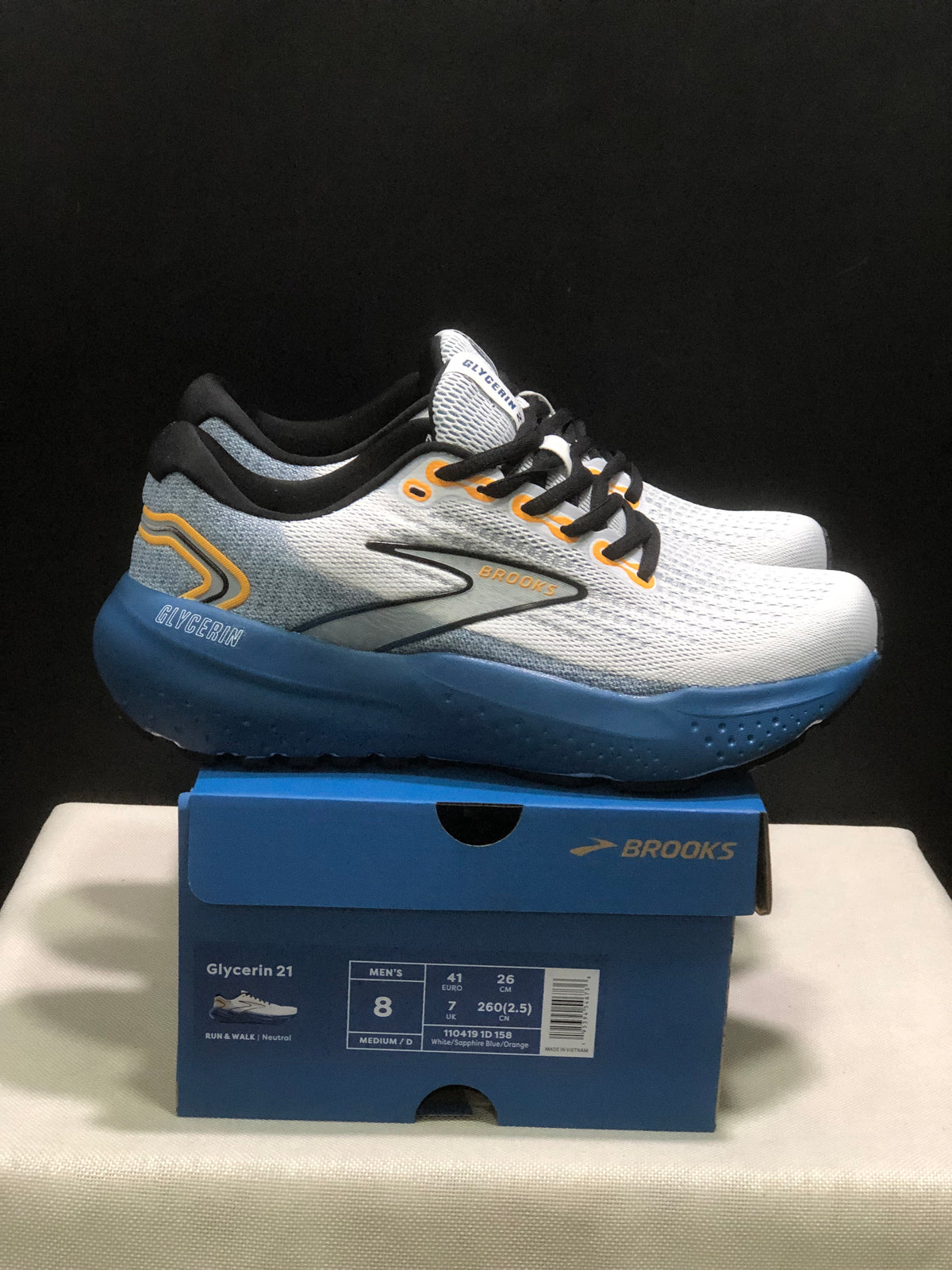 Side view of the white and blue Brooks Glycerin 21 sneakers with orange accents, displayed on a Brooks shoebox.