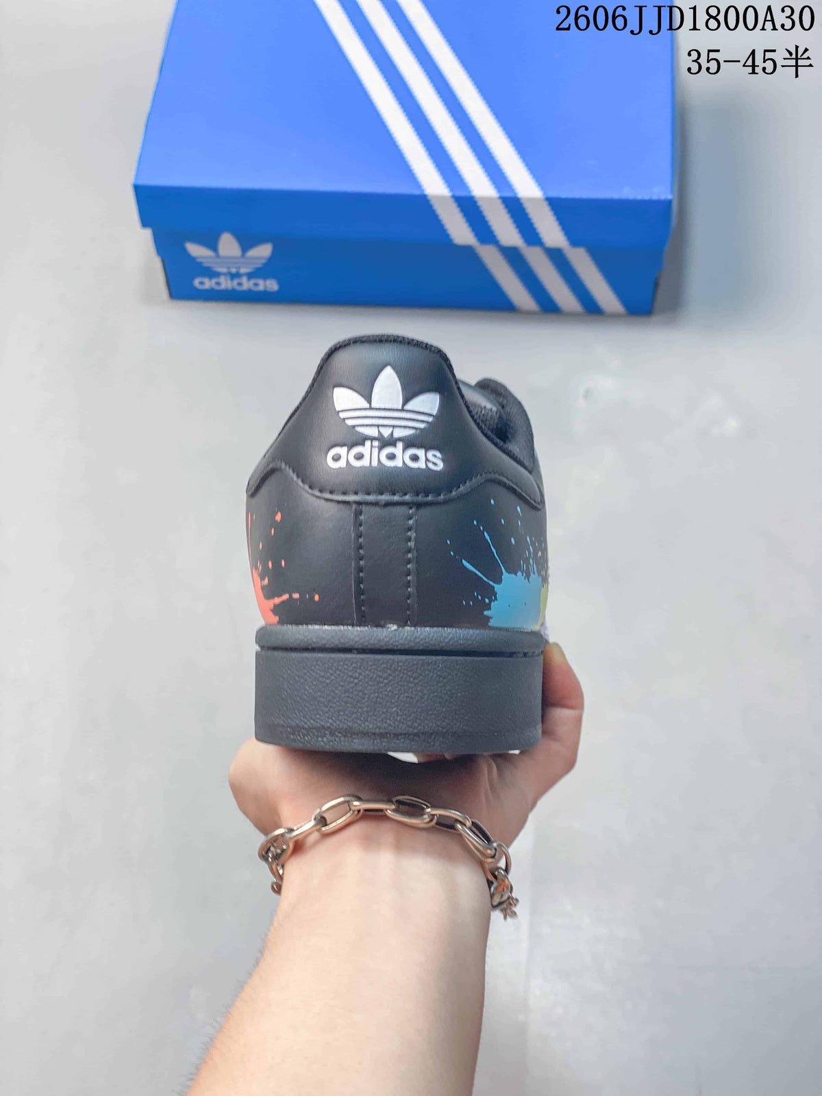 Rear view of the sneaker showing a trefoil heel logo and colorful splatter details.
