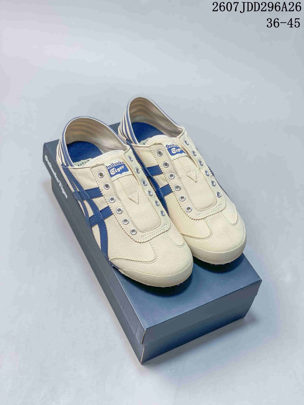 Pair of cream and navy Onitsuka Tiger Mexico 66 slip-on sneakers displayed on a shoebox; image text shows model code 2607JDD296A26 and size range 36-45.