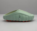 Side profile of a light green Nike slide showing the perforated upper, silver Swoosh-style emblem, and orange outsole elements.