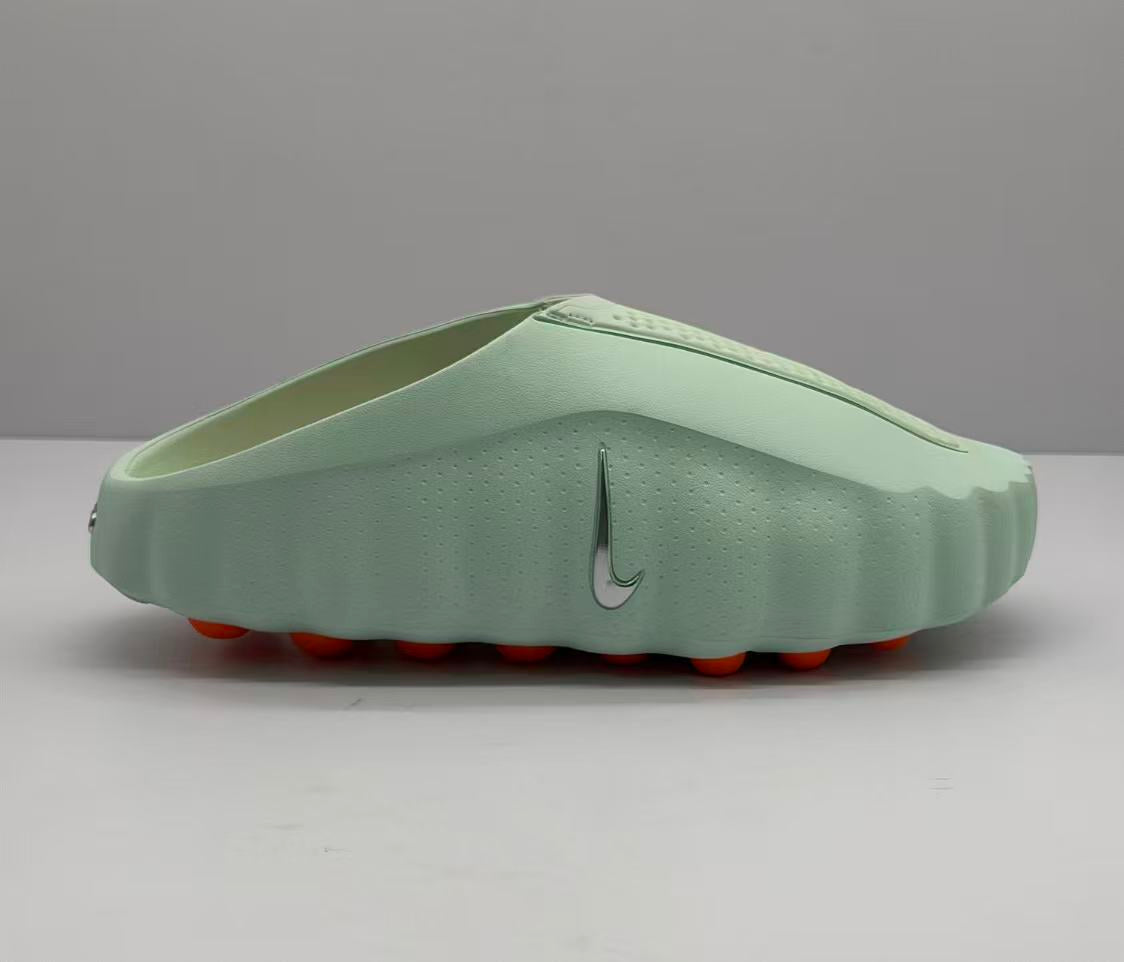 Side profile of a light green Nike slide showing the perforated upper, silver Swoosh-style emblem, and orange outsole elements.