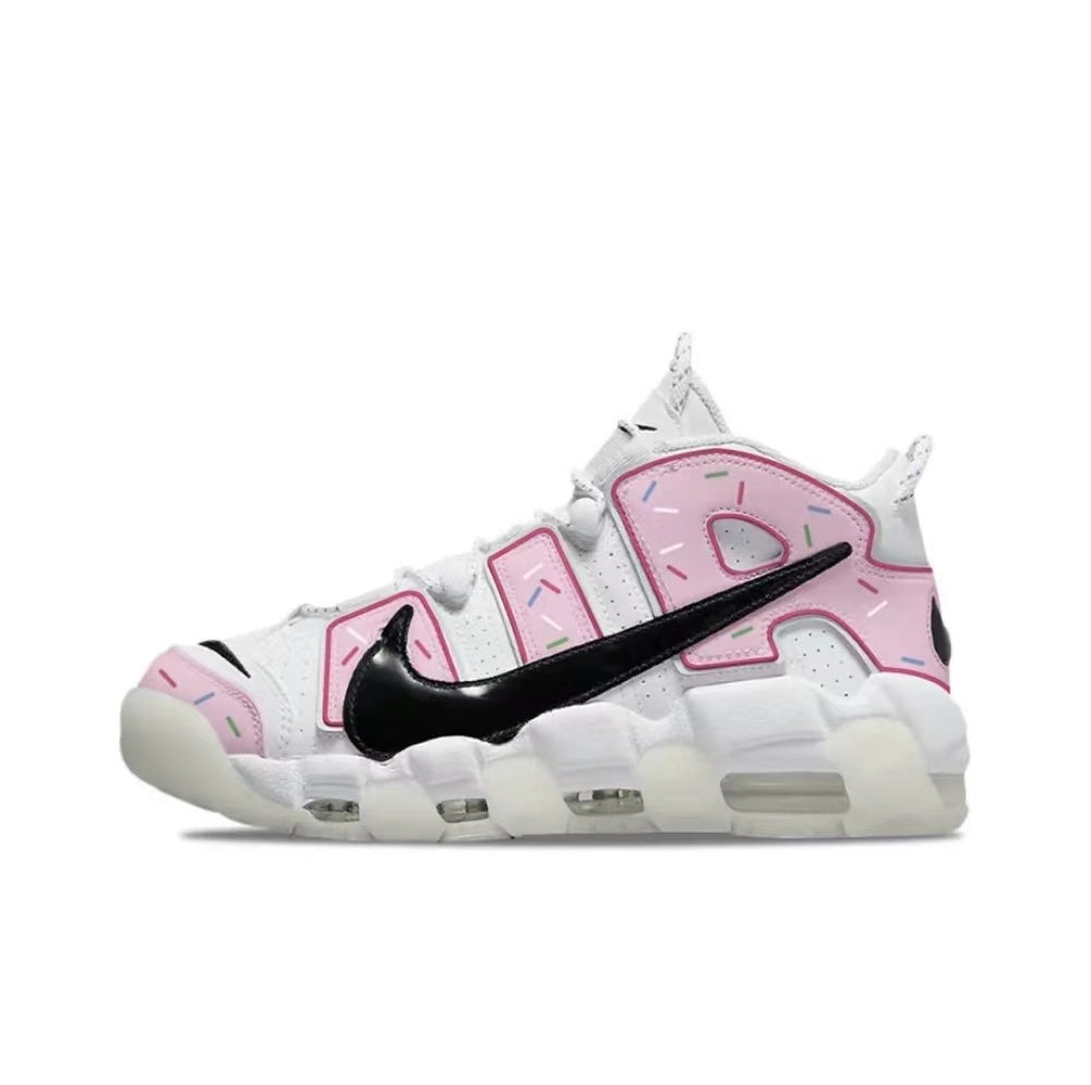 Side view of white Nike Air More Uptempo sneakers with pink donut-inspired lettering, colorful sprinkle details, a black Swoosh and a segmented white sole.