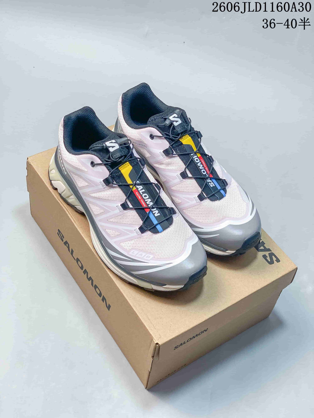 Pair of pale pink, gray, and navy Salomon XT-6 sneakers on a branded box