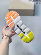 Underside view of the sneaker showing a segmented white outsole with orange and neon yellow-green traction sections.