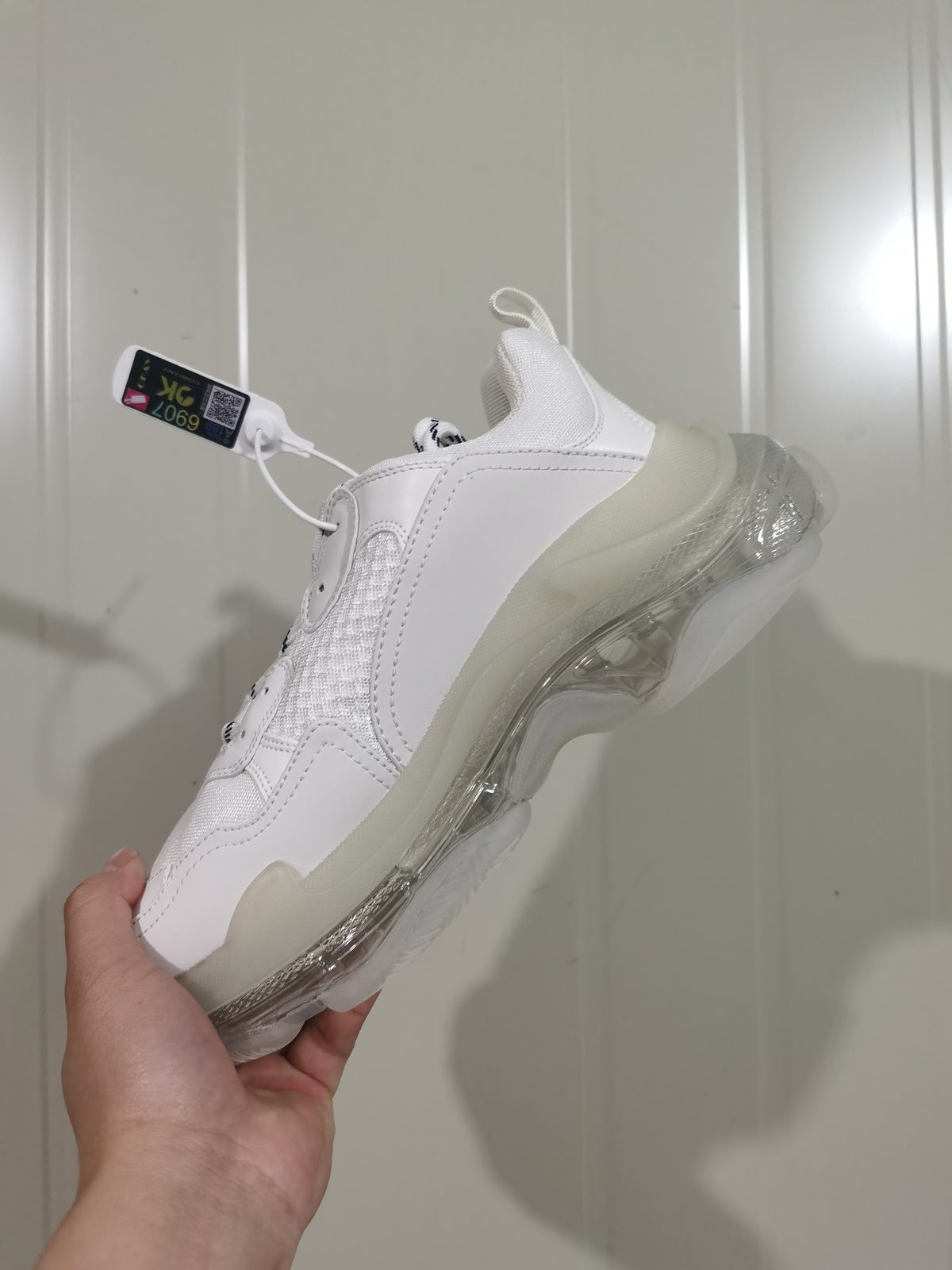 Angled rear-side view of the white sneaker showing the heel structure, stitched panels, pull tab, and translucent sole.