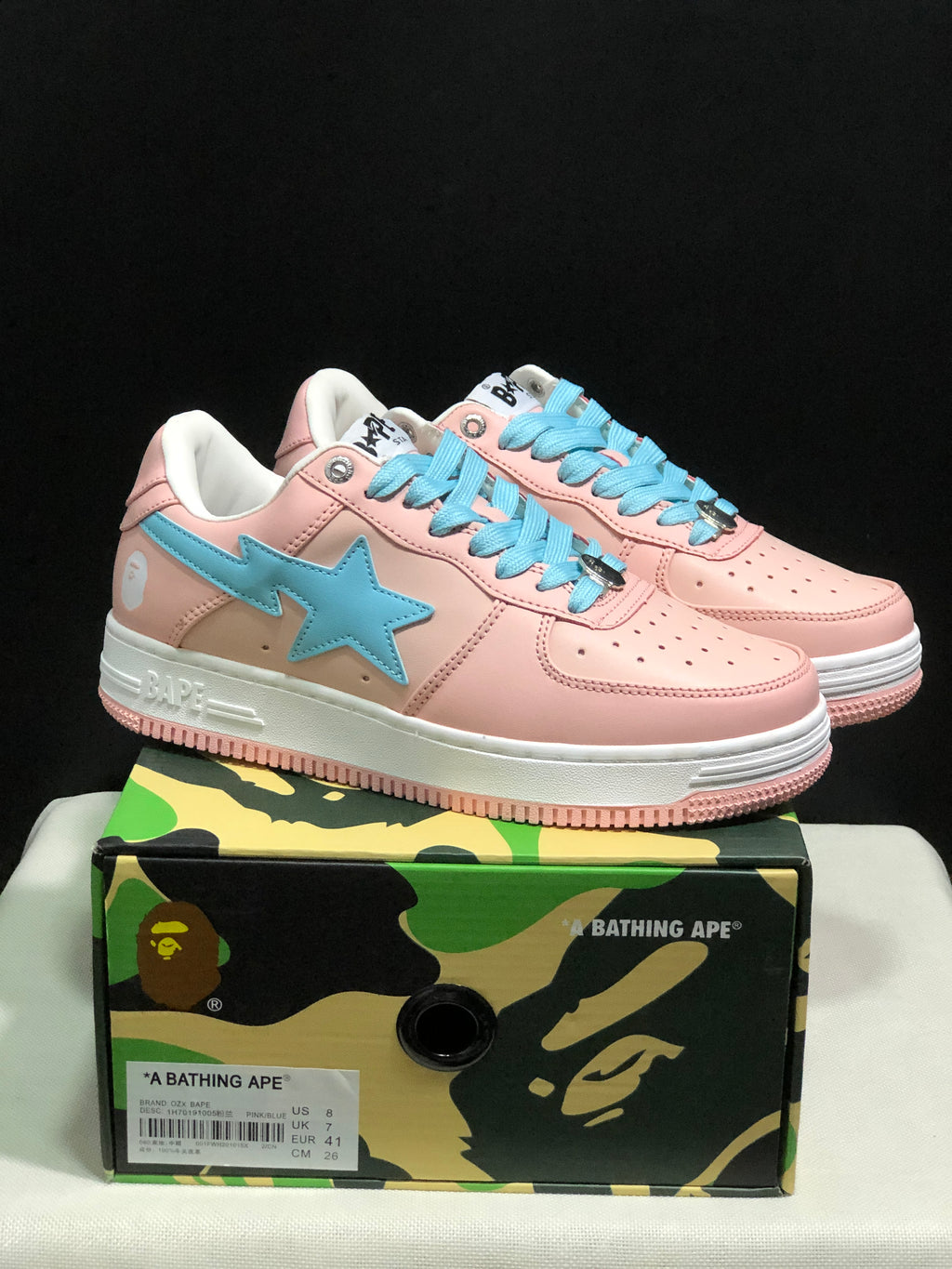 Pair of pink and light-blue Bape Sta low-top sneakers displayed on a camouflage Bape-branded shoe box; the box label visibly shows EU 41, US 8, UK 7, and CM 26.