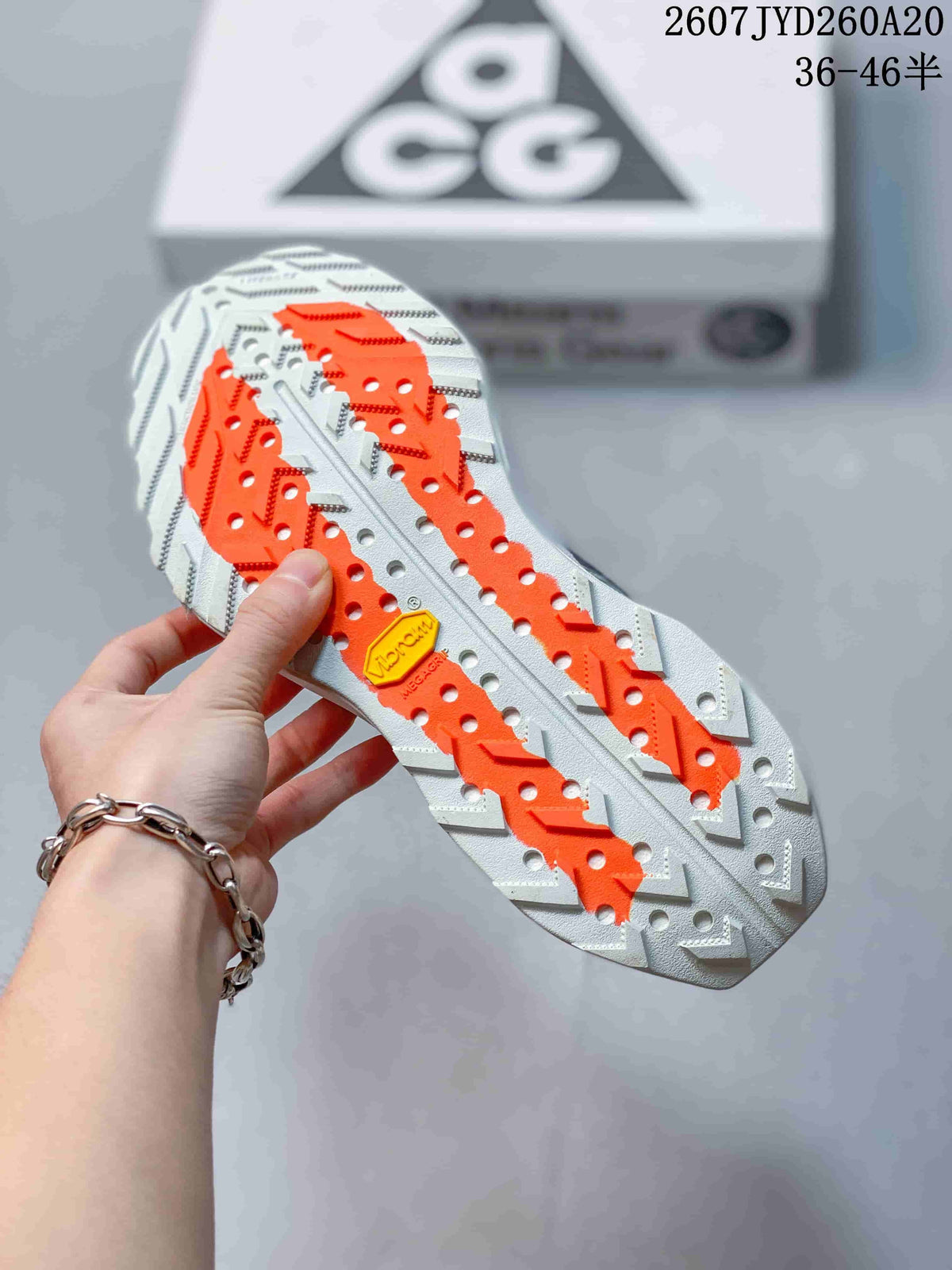 Close-up of the sneaker outsole showing white and bright orange traction elements, with an ACG shoebox in the background.