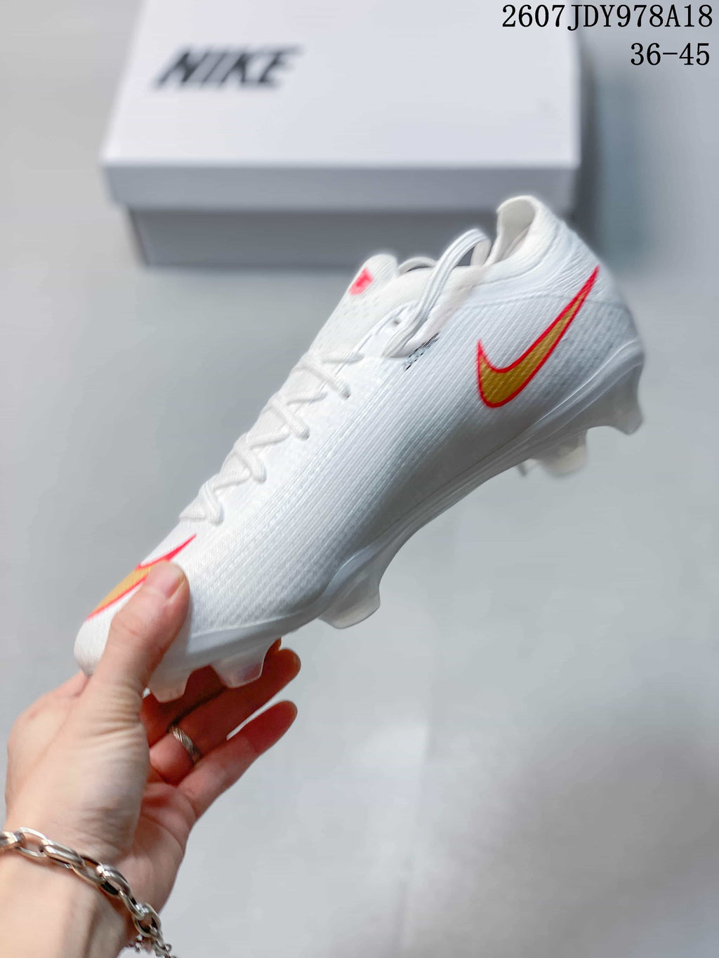 Side profile of the white Nike soccer cleat showing the gold and red Swoosh and molded outsole studs.