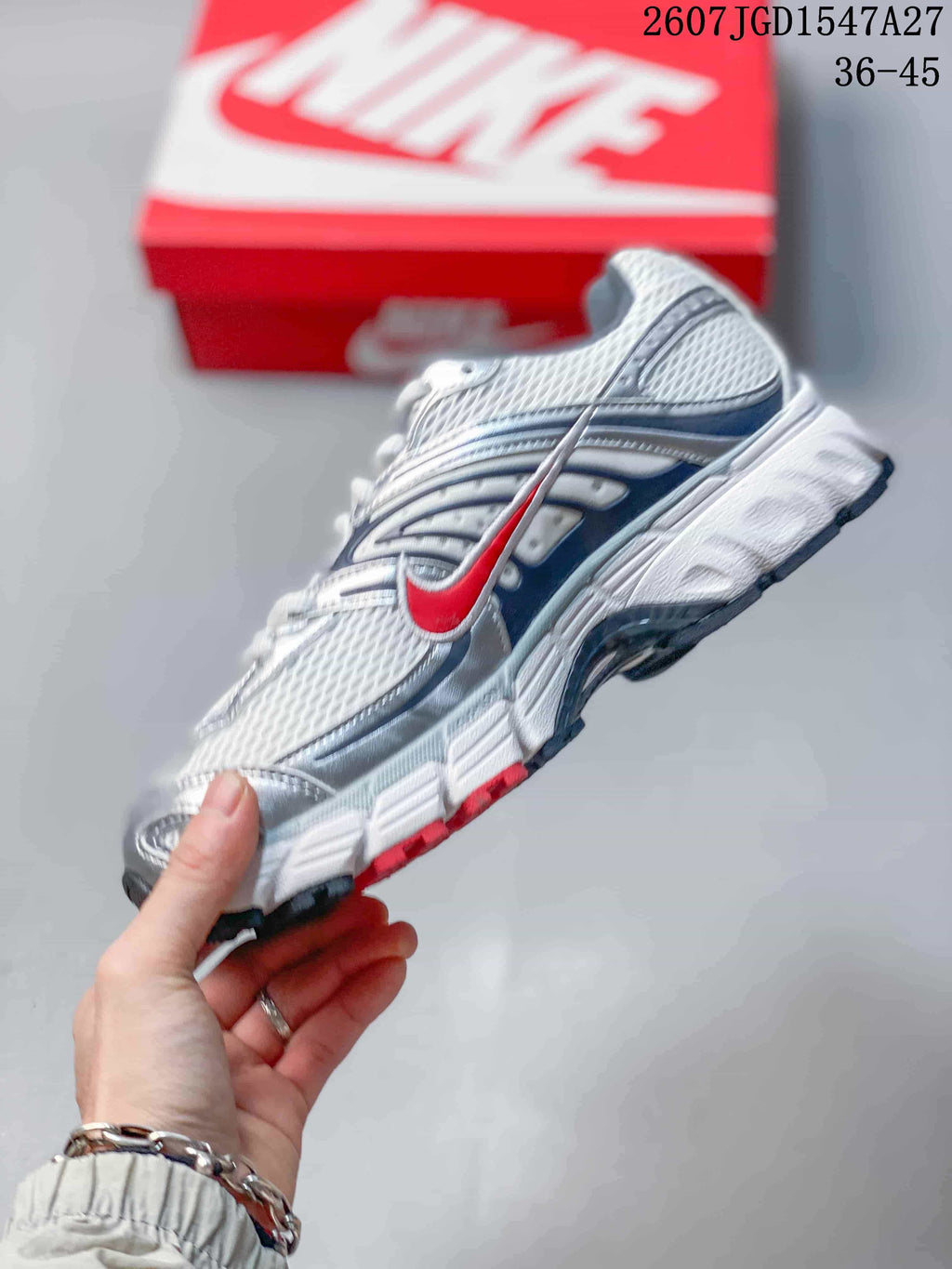 Side profile of a Nike Air Max Moto 2K sneaker showing the mesh upper, layered panels, and red accent details.