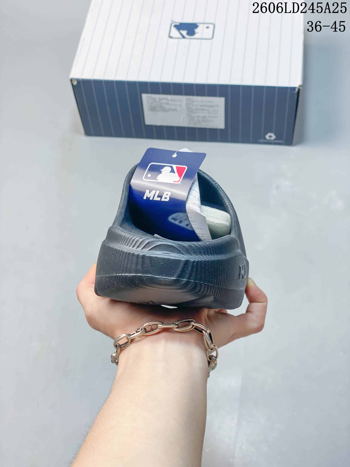 Rear view of a black MLB slide sandal with the raised heel section and MLB-branded packaging in the background.