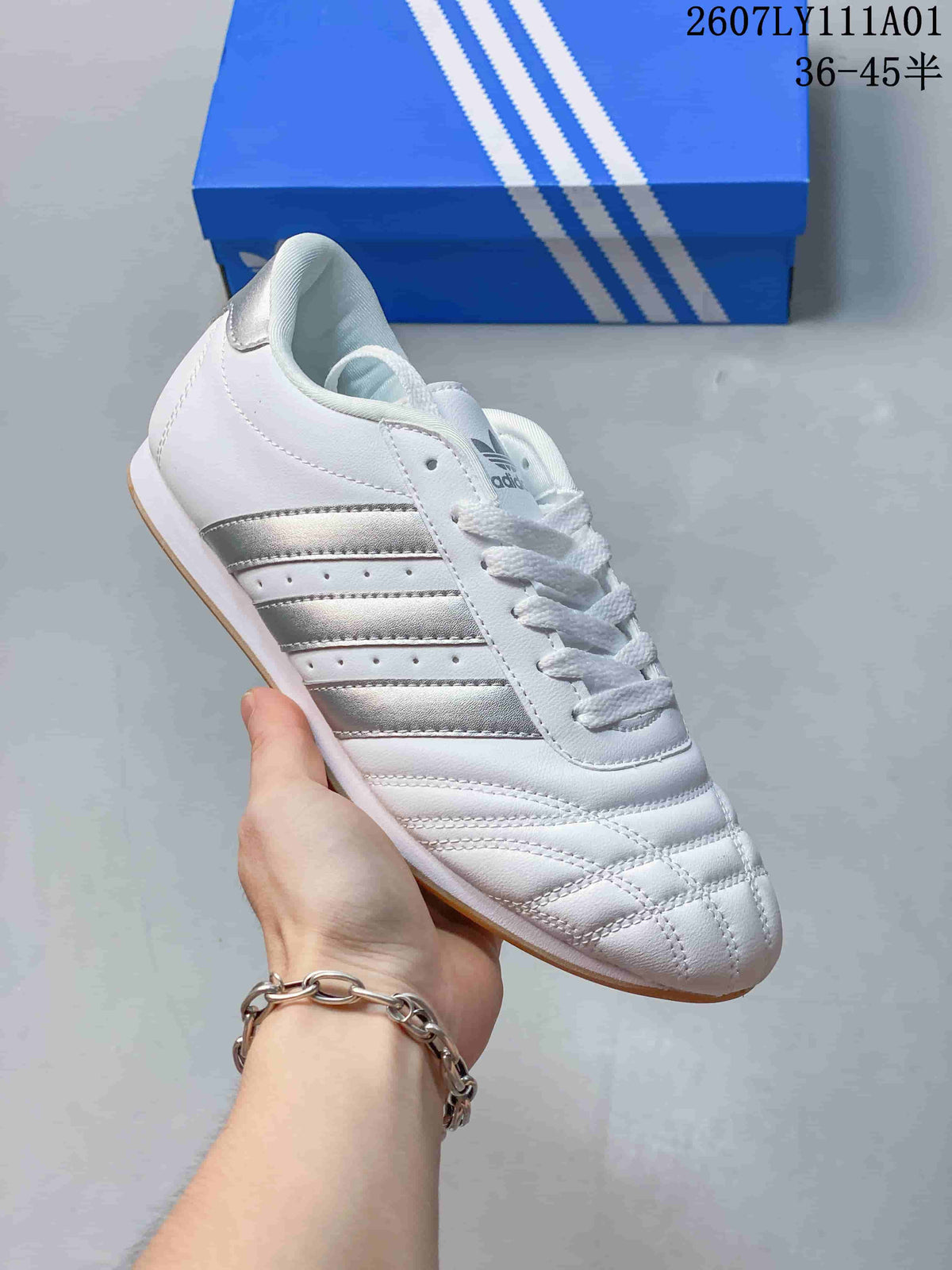 White Adidas Taekwondo low-top lace-up sneaker with metallic silver stripes.