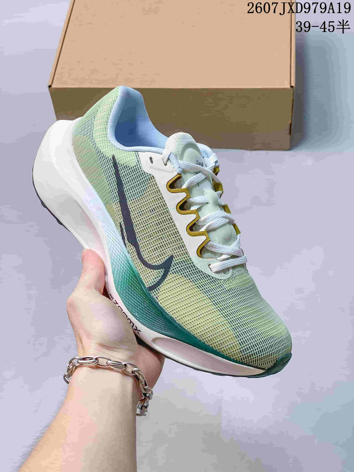 Light-colored Nike Zoom Fly 5 PRM sneaker with dark branding, gold-toned lace details and green-blue sole accents.
