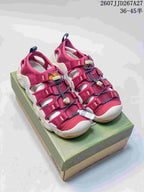 Pair of burgundy KEEN outdoor sandals with light midsoles on a KEEN shoe box; style code and size range text are visible at the top.